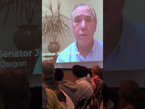 Oregon 9/11 commemoration video preview showing Senator Jeff Merkley on a screen above attendees